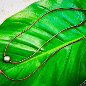 Full-length view of the leather choker necklace with its main Tahitian pearl and adjustment pearl displayed on a green leaf