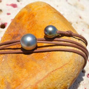 Close-up of the round 13 mm Tahitian pearl and adjustment pearl of the leather necklace displayed on a yellow rock