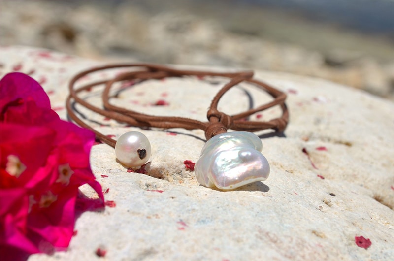 Close-up of the large baroque freshwater pearl, adjustment pearl and brown leather setting of the necklace on a rock