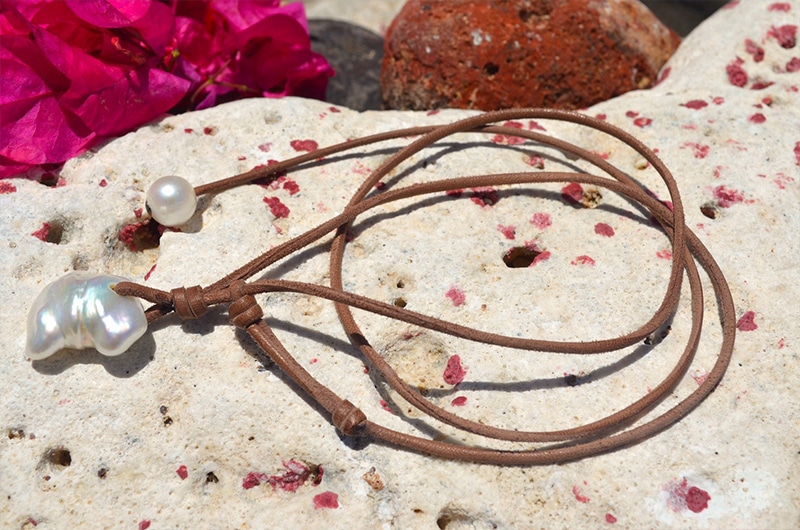 Detail of the two baroque freshwater pearls and knots of the leather necklace displayed near pink flowers