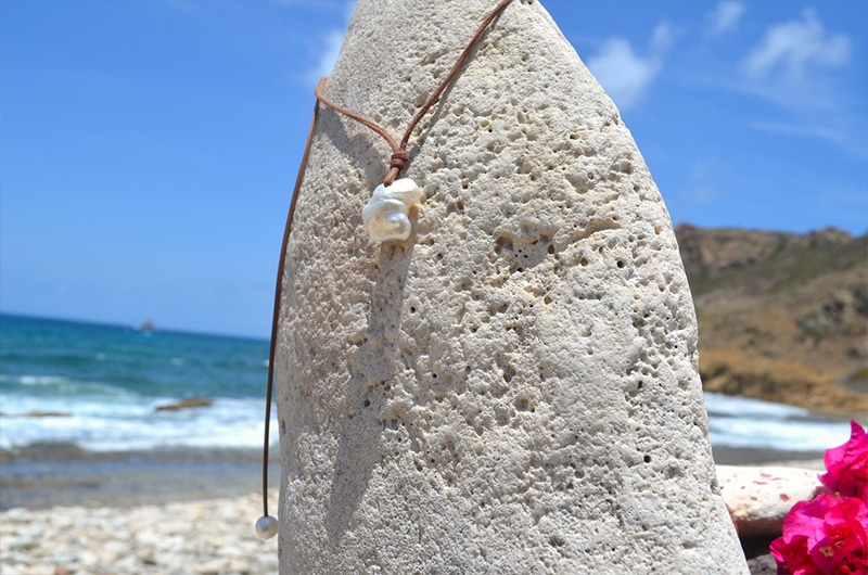 Leather pendant necklace with a large baroque freshwater pearl displayed vertically on coral at the beach
