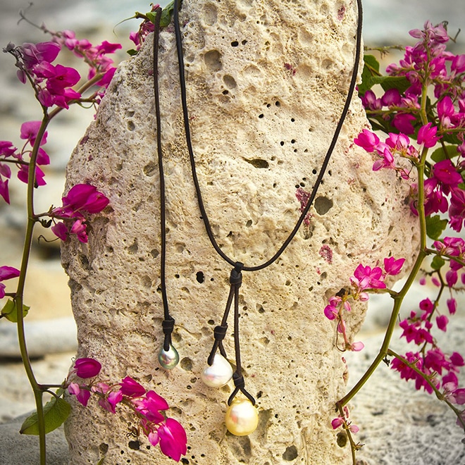 Collier grappe ajustable en cuir avec une perle blanche et une perle dorée d’Australie ainsi qu’une perle de Tahiti présenté à la plage