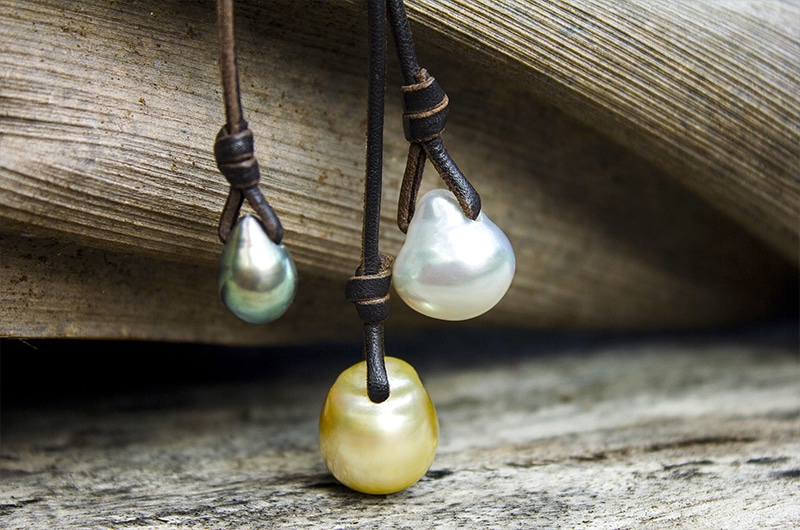 Gros plan sur les trois perles baroques blanche, dorée et de Tahiti du collier grappe présentées sur du bois