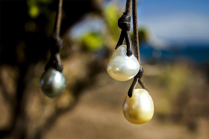 Collier grappe avec trois perles de culture blanche, dorée et de Tahiti présenté verticalement face à la mer