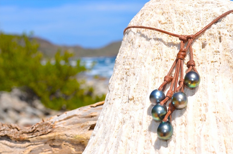 Gros plan sur les cinq perles principales de Tahiti, la perle d’ajustement et le montage en cuir du collier sur du bois
