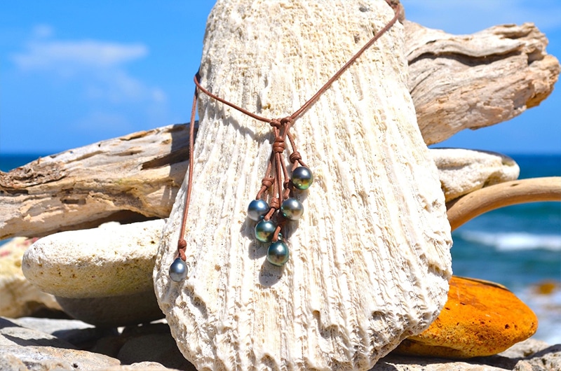 Vue d’ensemble du collier grappe ajustable en cuir avec cinq perles principales et une perle d’ajustement de Tahiti présenté à la plage