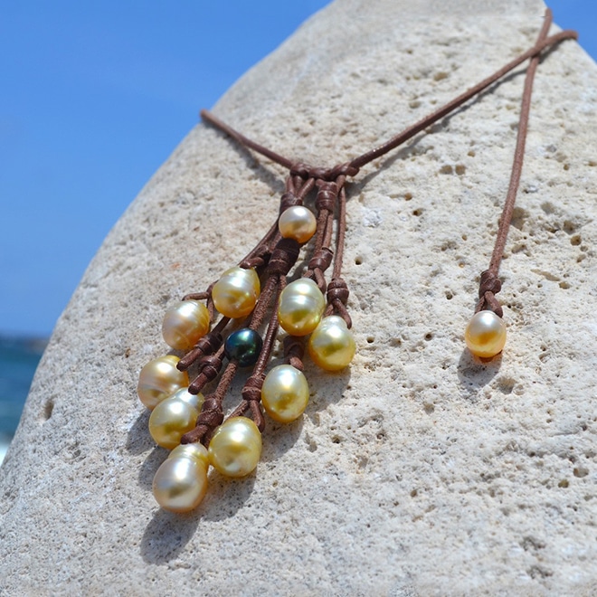 Adjustable leather cluster necklace with ten golden Australian pearls and a Tahitian accent pearl displayed facing the sea