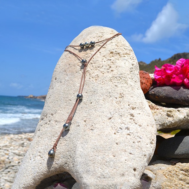 Full view of the adjustable leather long necklace with seven Tahitian cultured pearls displayed on coral at the beach