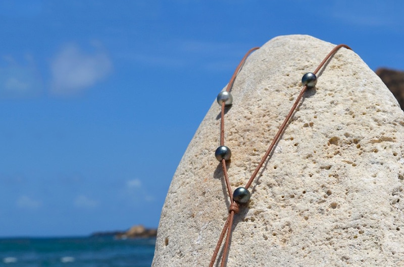 Alternate view of the adjustable long necklace with seven Tahitian pearls displayed on coral facing the sea