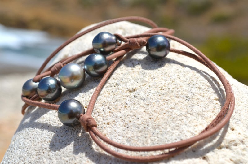Detail of the seven Tahitian cultured pearls and adjustable brown leather setting of the long necklace coiled on a rock