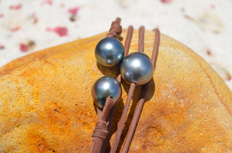Détail des trois perles de Tahiti semi-baroques et du montage en cuir marron du sautoir sur une roche