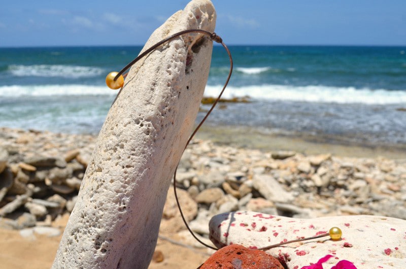 Vue latérale du collier ajustable en cuir avec ses deux perles dorées des mers du Sud face à la mer