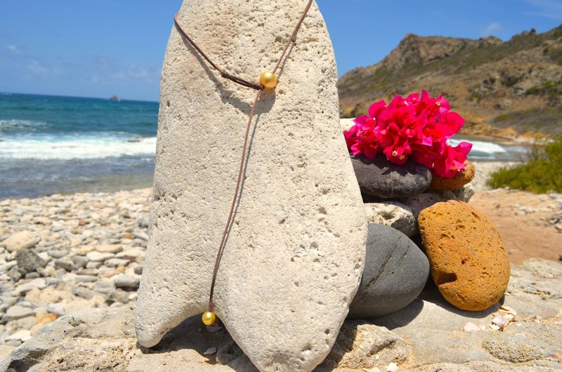 Vue d’ensemble du collier ras du cou en cuir avec deux perles dorées des mers du Sud présenté sur un support corallien à la plage