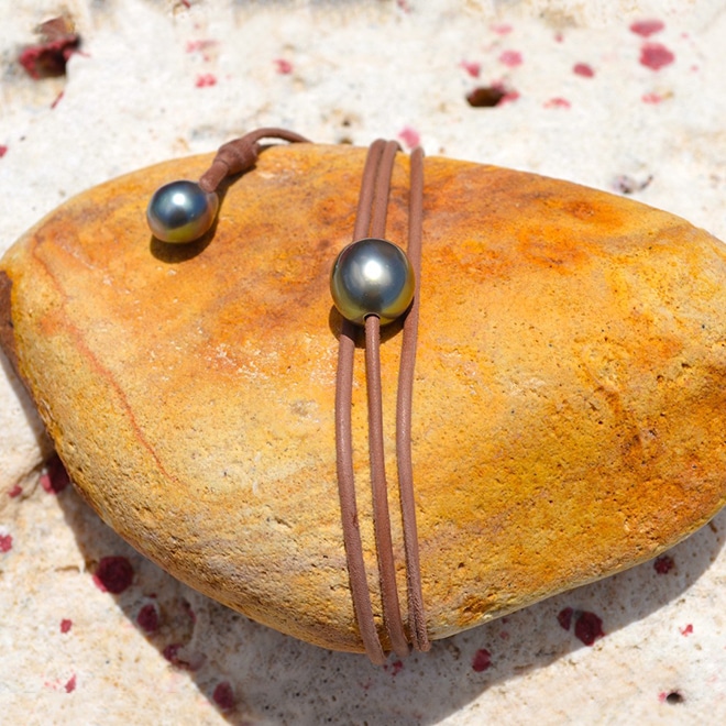 Collier ras du cou ajustable en cuir avec une perle principale de Tahiti ronde de 11 mm et une perle d’ajustement présenté sur une roche jaune