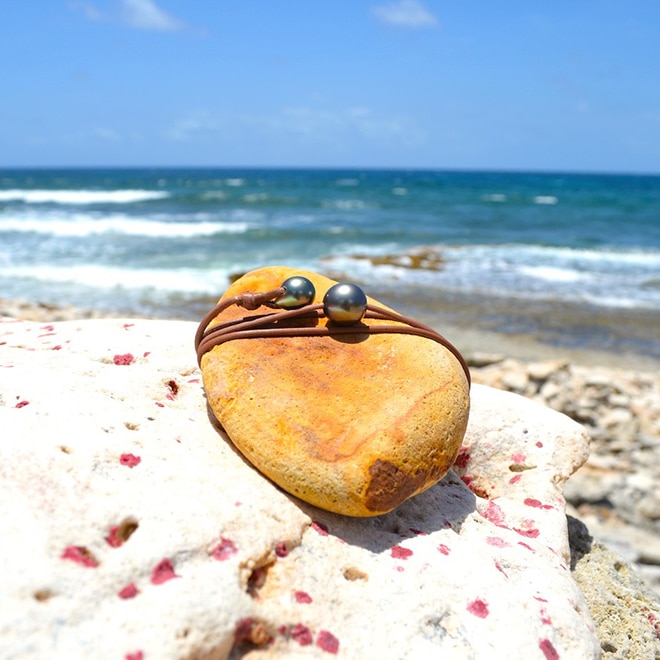 Adjustable leather choker with a 12 mm semi-round Tahitian main pearl and an adjustment pearl displayed on a rock
