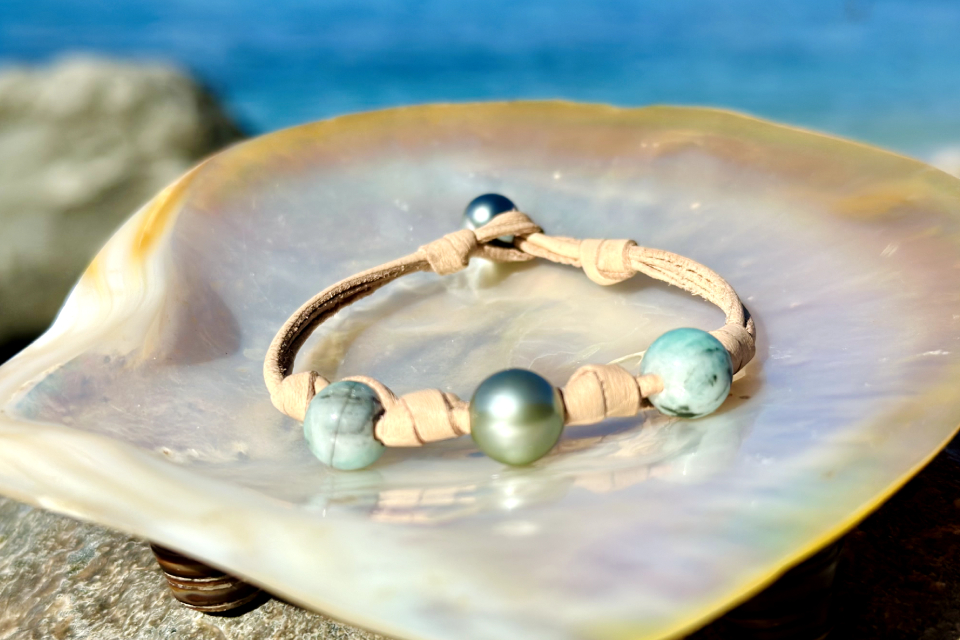Beige leather bracelet with emerald beads and a cultured pearl with green overtones displayed on mother-of-pearl