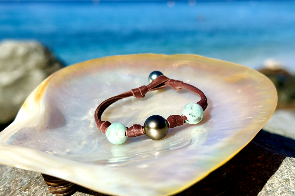 Brown leather bracelet with emerald beads and a dark Tahitian cultured pearl displayed on mother-of-pearl