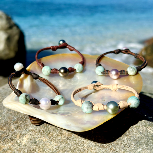 Selection of leather bracelets with emerald beads and cultured pearls in different colors displayed on mother-of-pearl