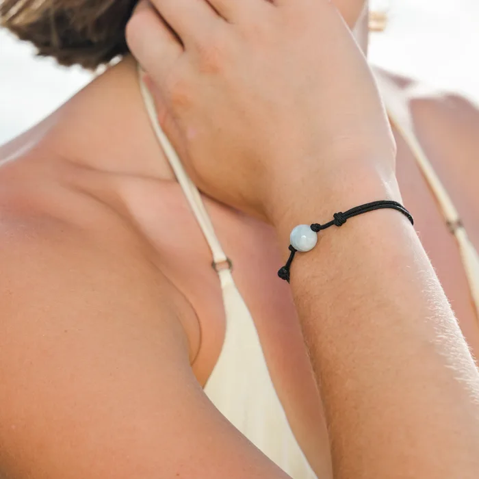 Close view of the adjustable bracelet with an aquamarine stone worn on the wrist against a beach background