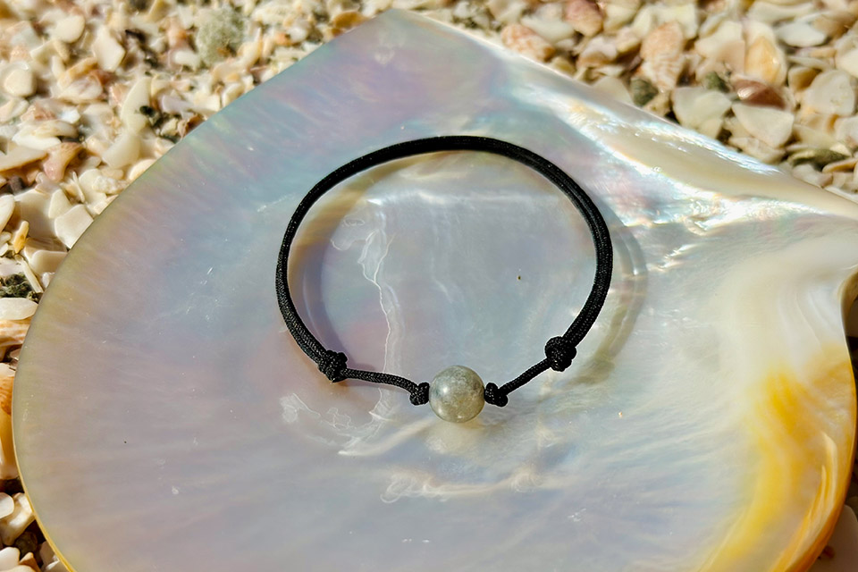 Adjustable brown cord bracelet with an 8 mm labradorite displayed on mother-of-pearl