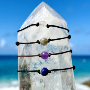 Quatre bracelets ajustables avec minéraux de 8 mm au choix présentés sur un cristal face à la mer