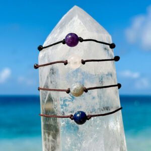 Quatre bracelets ajustables avec améthyste, lapis-lazuli, aigue-marine et labradorite de 10 mm présentés sur un cristal face à la mer