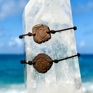 Deux bracelets ajustables avec anciennes monnaies en cuivre dites pièces de pirate présentés sur un cristal face à la mer