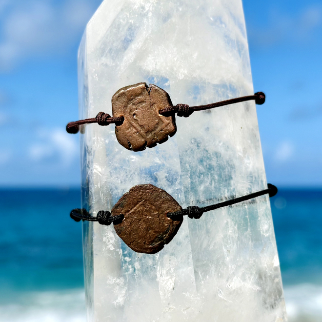 Two adjustable bracelets with antique copper coins known as pirate coins displayed on a crystal facing the sea