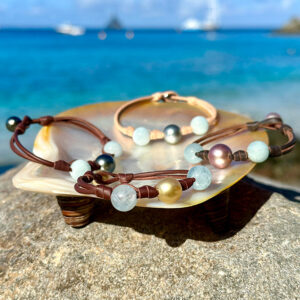 Ensemble de bracelets en cuir avec aigue-marine et perles de culture de différentes couleurs présenté sur une nacre face à la mer