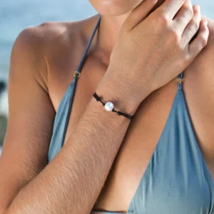 Bracelet ajustable sur cordon noir avec une perle de culture d’eau douce semi-ronde blanche porté au poignet à la plage