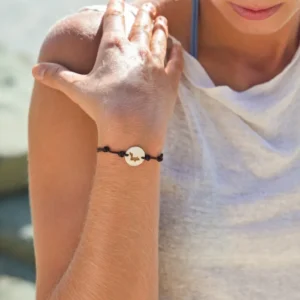 Adjustable brown cord bracelet with a golden mother-of-pearl Saint-Barthélemy silhouette worn on the wrist
