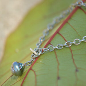 Bracelet chaîne en argent 925 avec une perle de Tahiti cerclée présenté sur une feuille verte