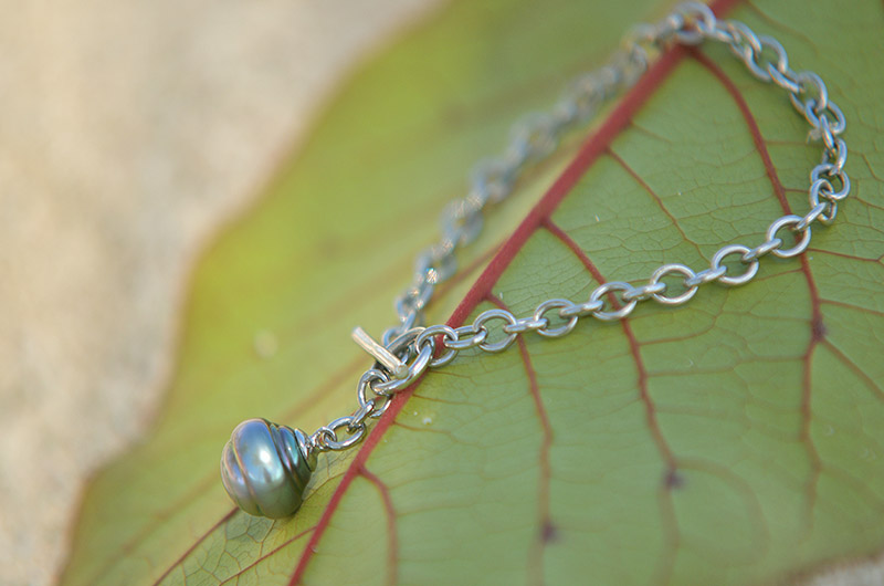 Bracelet chaîne en argent 925 avec une perle de Tahiti cerclée présenté sur une feuille verte