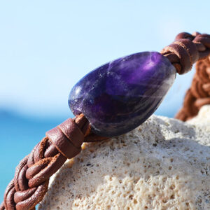 Gros plan sur l’améthyste, la perle de culture d’Australie et le cuir marron tressé du bracelet face à la mer