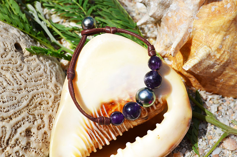 Bracelet avec une perle de Tahiti et quatre améthystes présenté dans un coquillage près de fleurs roses