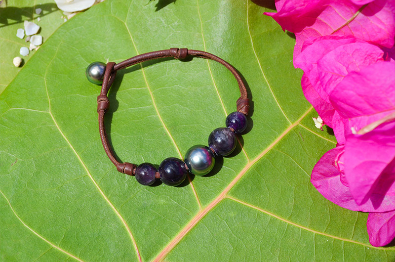 Bracelet en cuir marron avec une perle de Tahiti et quatre améthystes présenté sur une feuille verte