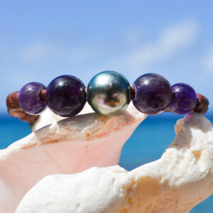 Bracelet en cuir marron avec une perle de culture de Tahiti et quatre améthystes présenté sur un coquillage face à la mer
