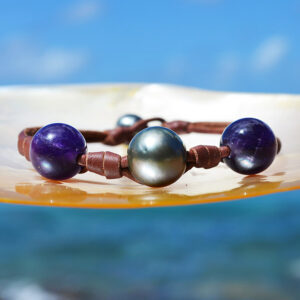 Bracelet en cuir marron avec nœuds, perles de culture de Tahiti et améthystes de 10 mm présenté face à la mer