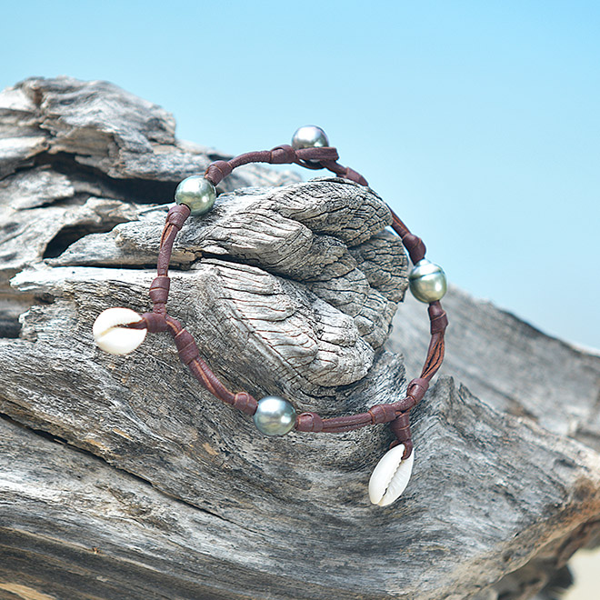 Leather bracelet or anklet with seashells and semi-baroque Tahitian cultured pearls displayed on wood
