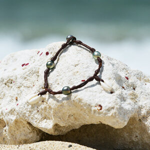 Bracelet ou chevillère en cuir avec coquillages et perles de Tahiti présenté sur une roche claire à la plage