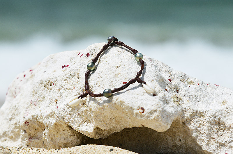 Leather bracelet or anklet with seashells and Tahitian pearls displayed on a pale rock at the beach