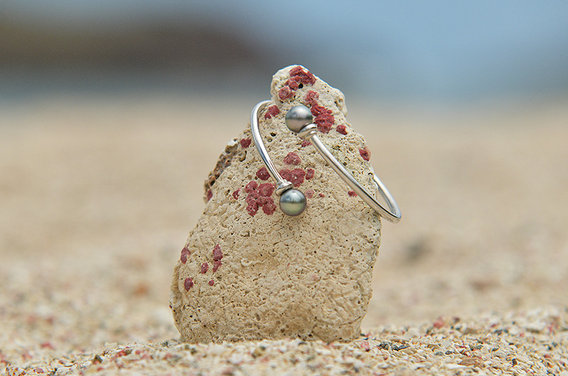 Bracelet jonc en argent 925 avec deux perles de Tahiti présenté sur une roche au bord de la mer