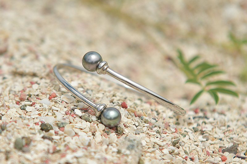 Bracelet jonc ouvert en argent 925 avec deux perles de Tahiti présenté sur le sable