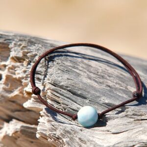 Bracelet ajustable en cuir marron avec une bille de Larimar de 10 mm présenté sur du bois flotté