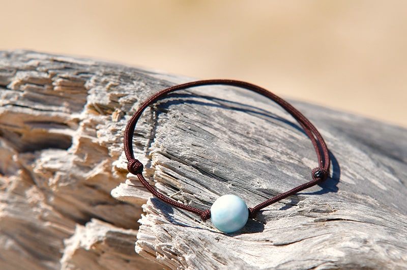 Adjustable brown leather bracelet with one 10 mm Larimar bead displayed on driftwood