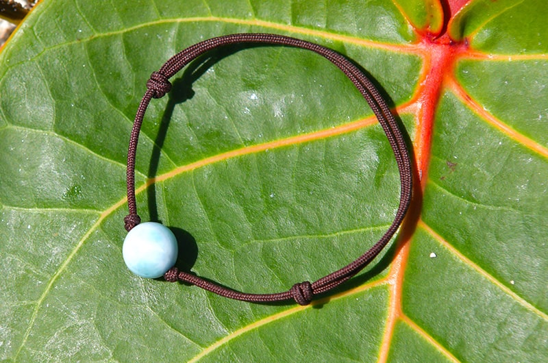 Adjustable brown cord bracelet with one Larimar bead displayed on a green leaf