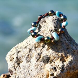 Vue d’ensemble du bracelet avec sept perles de Tahiti et Larimar présenté sur une roche face à la mer
