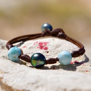 Bracelet en cuir marron avec nœuds, une perle de culture de Tahiti et deux éléments de Larimar présenté sur une roche