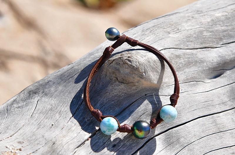 Brown leather bracelet with one Tahitian pearl and Larimar displayed on driftwood