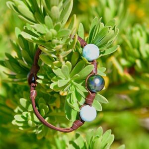 Bracelet en cuir avec une perle de Tahiti et deux éléments de Larimar présenté dans un feuillage vert
